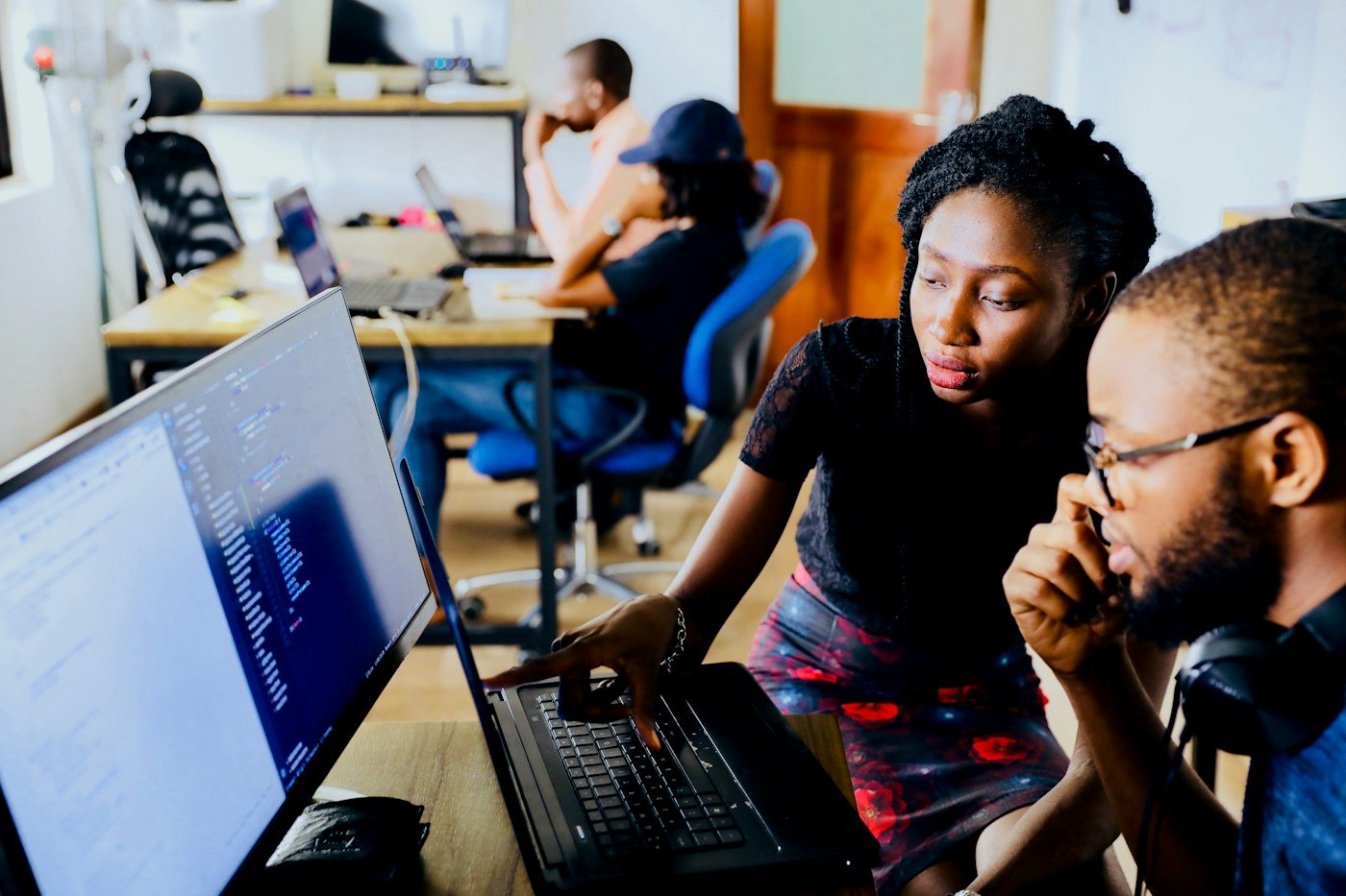 Two people at a desk, one pointing at a laptop screen full of code