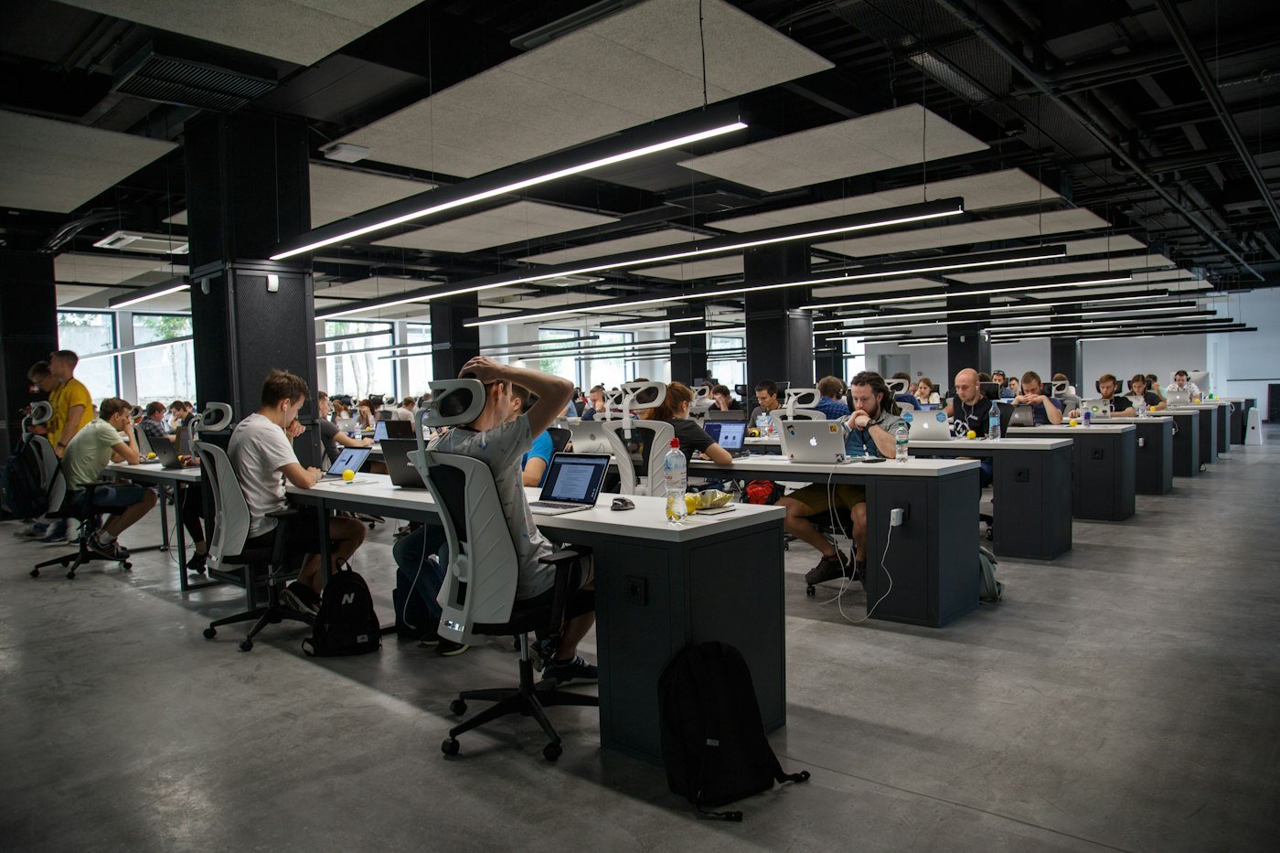 Rows of desks in a dark open office, each with a laptop open