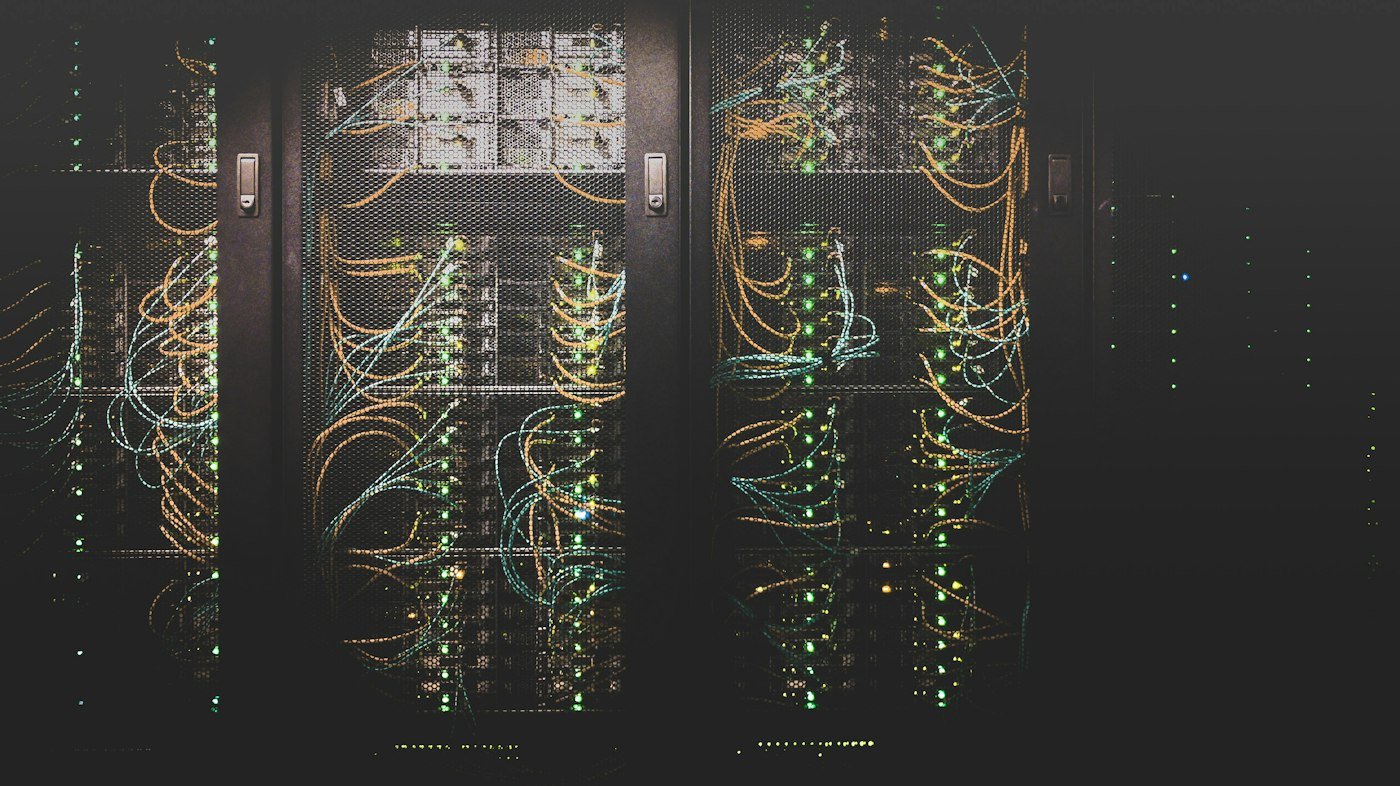 Server racks behind mesh doors, with green lights and bundles of network cables